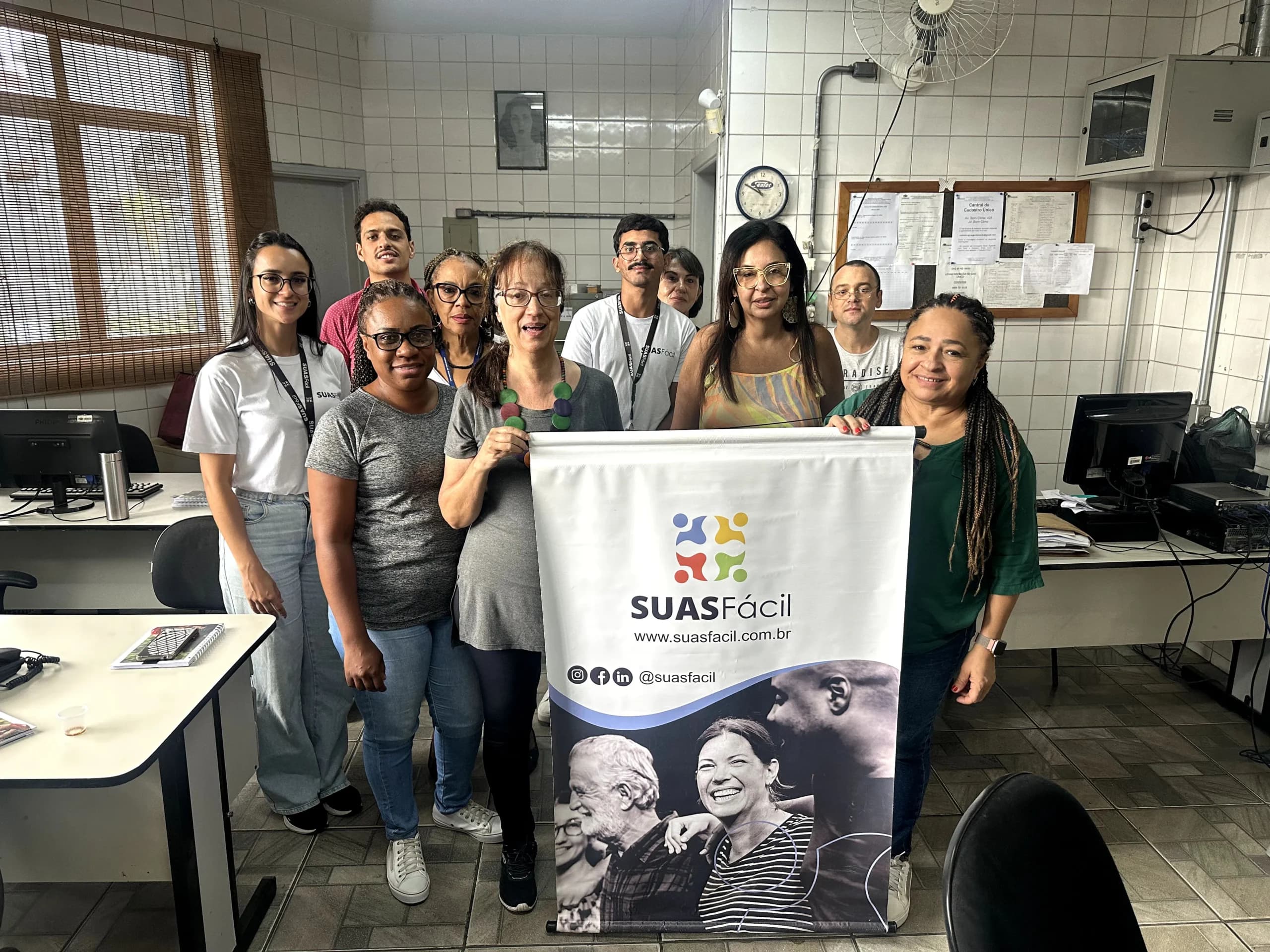 Equipe do SUAS Fácil reunida ao lado do banner da marca